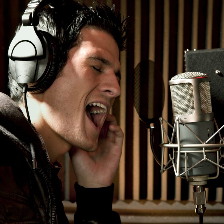 This photo shows a young man singing into a studio mic, wearing headphones